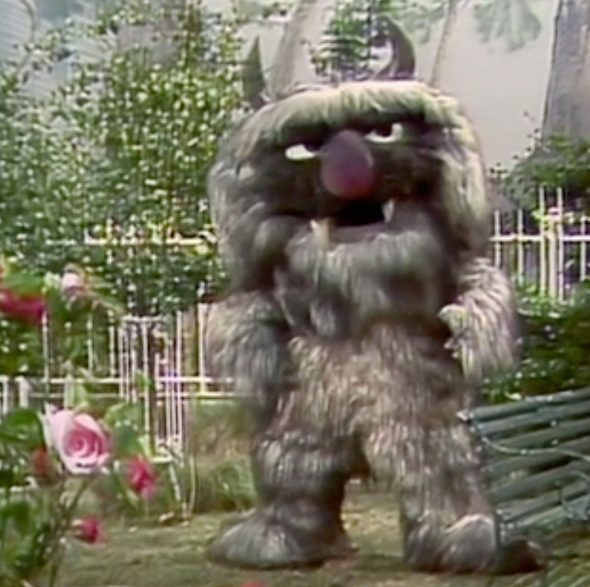 Doglion, a large, shaggy Muppet monster, stands in a park.