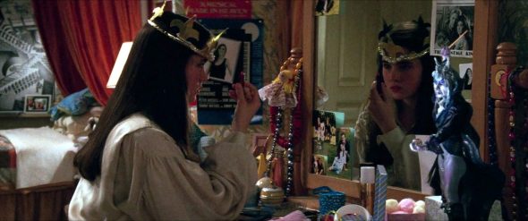 Screenshot from Labyrinth: Sarah putting on lipstick in the mirror with a photo of David Bowie's Jeremy on it. In front of the mirror is a statue of the Goblin King.